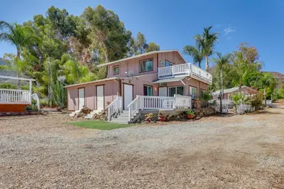 a large pink house with white railings and trees at 4 Mi to Shore Lake Elsinore Studio with Mtn Views in Lake Elsinore