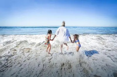 a man and two children walking in the water on the beach at 6Br Oceanview Getaway Steps From 27Th St Beach By Beachview Rentals in Newport Beach