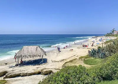 a beach with a straw umbrella and a crowd of people at La Jolla Village Escape - Walk to Everything in San Diego