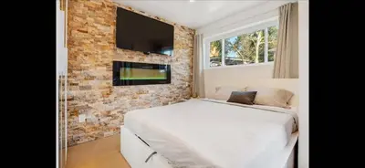 a bedroom with a white bed and a tv on a brick wall at Mission Beach Suite Parking Steps 2 Ocean in San Diego