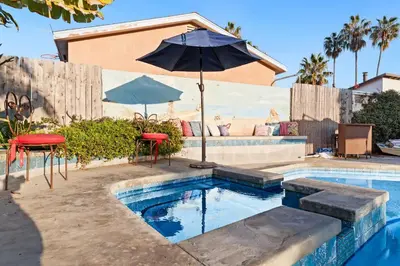 a pool with an umbrella and two chairs and a table at Stay & Play Pacific Beach Compound in San Diego