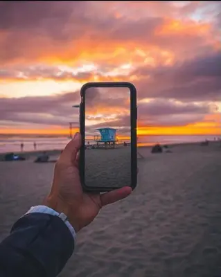 a person holding up a cell phone to take a picture of the beach at 5N-31 Beach View BBQ & Jacuzzi in Oceanside