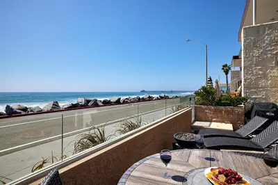 a table with a plate of food on a balcony with the beach at 700-104 Water Front Condo w AC in Oceanside