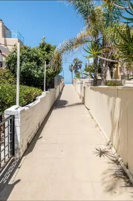 a sidewalk with a fence and palm trees and the ocean at Roswitha's Blue Wave Cottage in San Diego