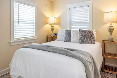 a bedroom with a white bed with two windows at Roswitha's Blue Wave Cottage in San Diego