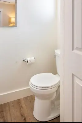 a white bathroom with a toilet and a roll of toilet paper at Roswitha's Blue Wave Cottage in San Diego