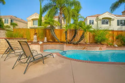 a swimming pool with two chairs in front of a fence at Peaceful Poolside Perfection near Wine Country in Murrieta