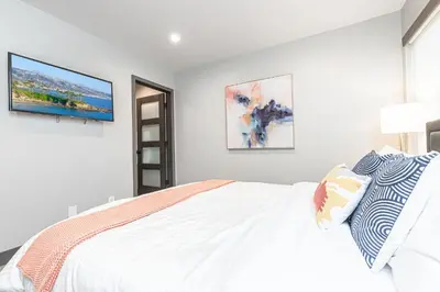 a white bedroom with a bed and a tv on the wall at 8Br Retreat With Ac, Modern Upgrades, And Two Rooftop Decks By Beachview Rentals in Newport Beach