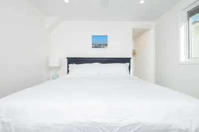 a white bed in a white bedroom with a window at Remodeled Oceanfront Home On The Boardwalk By Beachview Rentals in Newport Beach