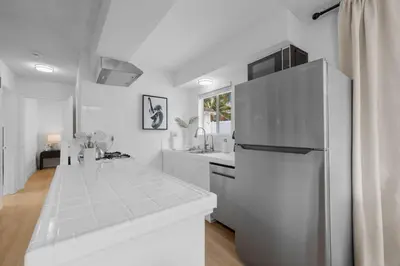 a white kitchen with a stainless steel refrigerator at Ocean Paradise | Patio, Parking, BBQ, Location! in San Diego