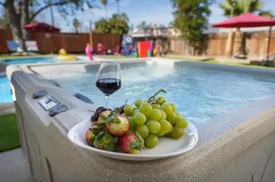 a plate of fruit and a glass of wine next to a swimming pool at Sleeps 12 - Hot Tub - Pool - Game Room & Fire Pit! in Hemet
