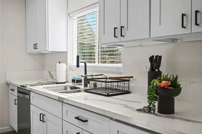 a kitchen with white cabinets and a sink and a window at Sleeps 12 - Hot Tub - Pool - Game Room & Fire Pit! in Hemet