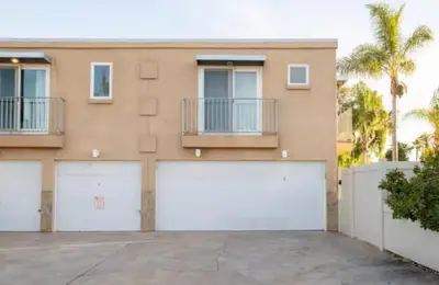 a house with two garage doors and a fence at Boho Chic Cottage Walk to Cafes Outdoor Lounge in San Diego