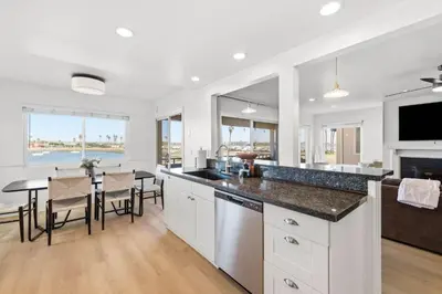 a kitchen with white cabinets and a dining room with a table at Remodeled 4BR Bayfront Home | Sleeps 12 | Stunning Views + BBQ Patio in San Diego