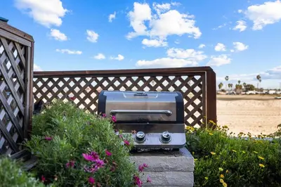 a grill sitting on a fence next to the beach at Bayfront Getaway | 2BR Retreat w/ Patio & BBQ, Steps to Sand in San Diego