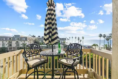 a patio table with two chairs and an umbrella on a balcony at Beachfront Resort-sunset views deck & luxe king in Oceanside