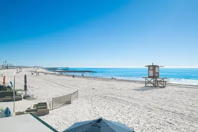 a sandy beach with an umbrella and the ocean at 3Br Oceanfront Home W Balcony Right Over The Sand By Beachview Rentals in Newport Beach