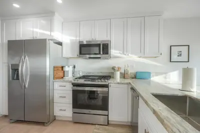 a kitchen with white cabinets and a stainless steel refrigerator at Modern Ocean-View Retreat w/ Firepit & Steps to Carlsbad Beach in Carlsbad
