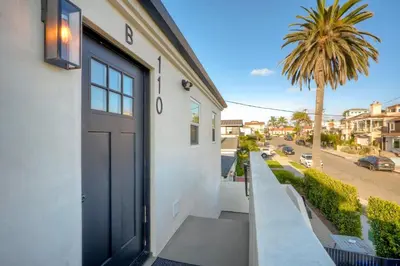 a door on a white building with a palm tree at Sycamore Haus Estate – Rent All 3 Ocean-View Luxury Condos Steps from Carlsbad State Beach in Carlsbad