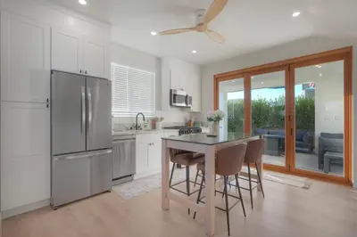 a kitchen with a refrigerator and a table with chairs at Luxury Carlsbad Retreat | Across The Street From Beach | Firepit, BBQ, Ping Pong, Cornhole & More in Carlsbad