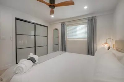 a white bedroom with a large bed and a ceiling fan at Luxury Carlsbad Retreat | Across The Street From Beach | Firepit, BBQ, Ping Pong, Cornhole & More in Carlsbad