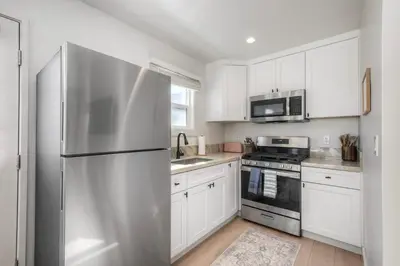 a kitchen with white cabinets and a stainless steel refrigerator at Modern Carlsbad Vacation Rental with Ocean Views, Private Patio, Fire Pit & Walkable Location in Carlsbad