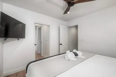 a bedroom with a white bed with a flat screen tv at Modern Carlsbad Vacation Rental with Ocean Views, Private Patio, Fire Pit & Walkable Location in Carlsbad