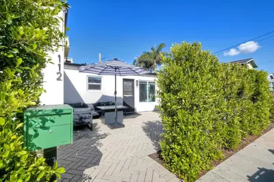a patio with a table and an umbrella and some bushes at Modern Carlsbad Vacation Rental with Ocean Views, Private Patio, Fire Pit & Walkable Location in Carlsbad