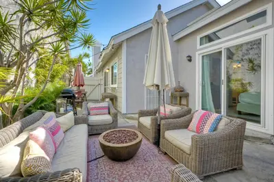 a patio with wicker furniture and an umbrella at Carlsbad Coastal Cottage — Private Patio + Gated Pool & Spa in Minutes to the Beach! in Carlsbad