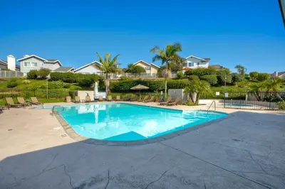 a large swimming pool with chairs and trees at Carlsbad Coastal Cottage — Private Patio + Gated Pool & Spa in Minutes to the Beach! in Carlsbad