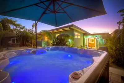 a hot tub with an umbrella in front of a house at Luxury 3-Bed Beach Cottage with Hot Tub, Fire Pit, BBQ - Walk To Beach in Cardiff-by-the-Sea
