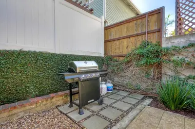 a barbecue grill in a yard next to a fence at Coastal Cottage Steps from the Sand | Walk to Carlsbad Village, Dog-Friendly in Carlsbad