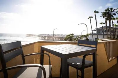 a table and chairs on a balcony with the beach at Pier View Sunset - Ocean Front, Patios, Location, Views in San Diego