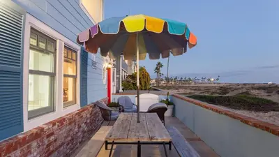 a wooden table with an umbrella on a patio at Oceanfront Atelier by AvantStay Beachfront Balboa Peninsula Escape in Newport Beach