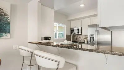 a kitchen with white cabinets and white stools at Seabright Sky by AvantStay Top-Floor West Newport Retreat • Balcony Near Beach Cafes in Newport Beach