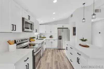 a white kitchen with white cabinets and a refrigerator at Poolside Paradise in Central SD in San Diego