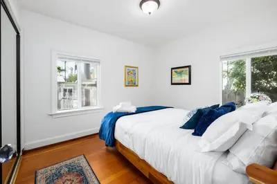 a white bedroom with a bed and two windows at Vintage Beach Bungalow in Oceanside