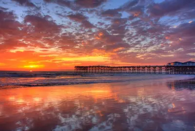 a beach with a pier at sunset with the ocean at The Seabreeze by Coastline Vacation Rentals in San Diego
