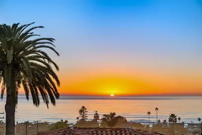 a palm tree on a beach with a sunset at Golden Hour by Coastline Vacation Rentals in Encinitas