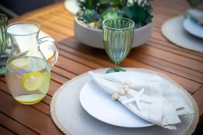 a table with a glass vase and a plate with a drink at PB Beach Compound - 2 New Homes Steps to Sand in San Diego
