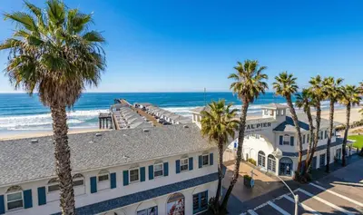 a building on the beach with palm trees and the ocean at Pier-View Penthouse Condo in Pacific Beach in San Diego