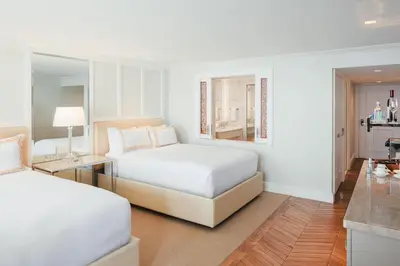 a white bedroom with two beds and a kitchen at Surf & Sand Laguna Beach in Laguna Beach
