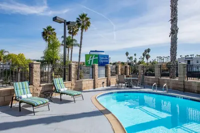 a swimming pool with chairs and a fence with palm trees at Holiday Inn Express San Diego South - National City by IHG in National City