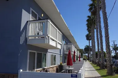 a blue building with a balcony and chairs and palm trees at Seaside Village Carlsbad in Carlsbad