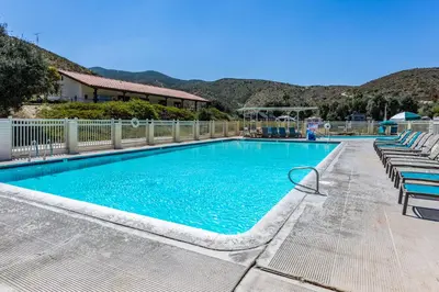 a large swimming pool with chairs and mountains in the background at Pio Pico Camping Resort One-Bedroom Cabin 14 in Jamul