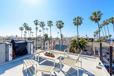 a patio with chairs and a table on a roof with palm trees at New Beach House, Steps to Sand in San Diego
