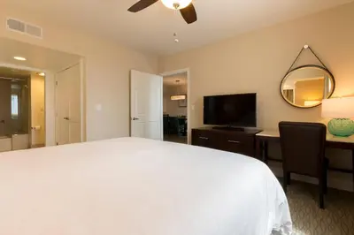 a bedroom with a white bed and a desk and a television at Carlsbad Seapointe Resort in Carlsbad