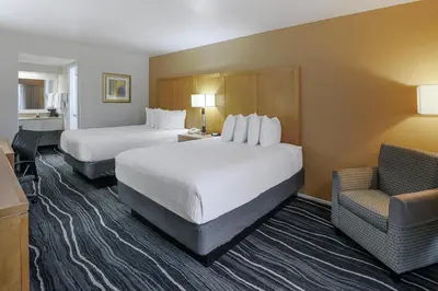a hotel room with two beds and a chair at Ramada by Wyndham Costa Mesa/Newport Beach in Costa Mesa