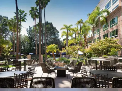 an outdoor patio with tables and chairs and palm trees at DoubleTree by Hilton San Diego Del Mar in San Diego