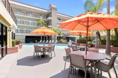 an outdoor patio with tables and umbrellas next to a pool at Best Western Plus Irvine Spectrum Hotel in Lake Forest